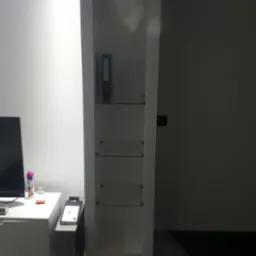 Wnęka z półkami szklanymi w ścianie, widoczny segregator na górnej półce, ciemna podłoga i słabe oświetlenie.