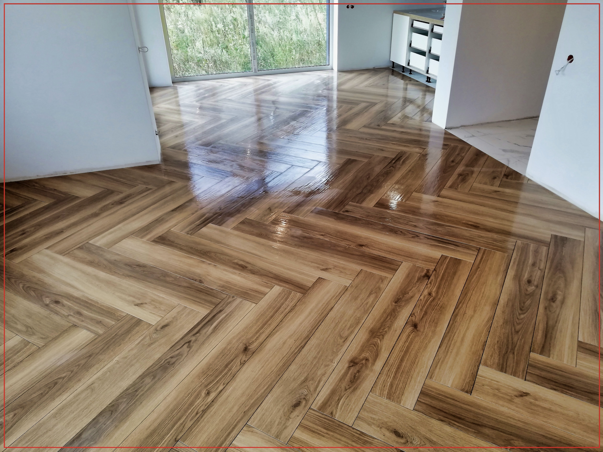 Ułożona w jodełkę, błyszcząca podłoga z płytek imitujących drewno w przestronnym wnętrzu, widok z niskiej perspektywy.