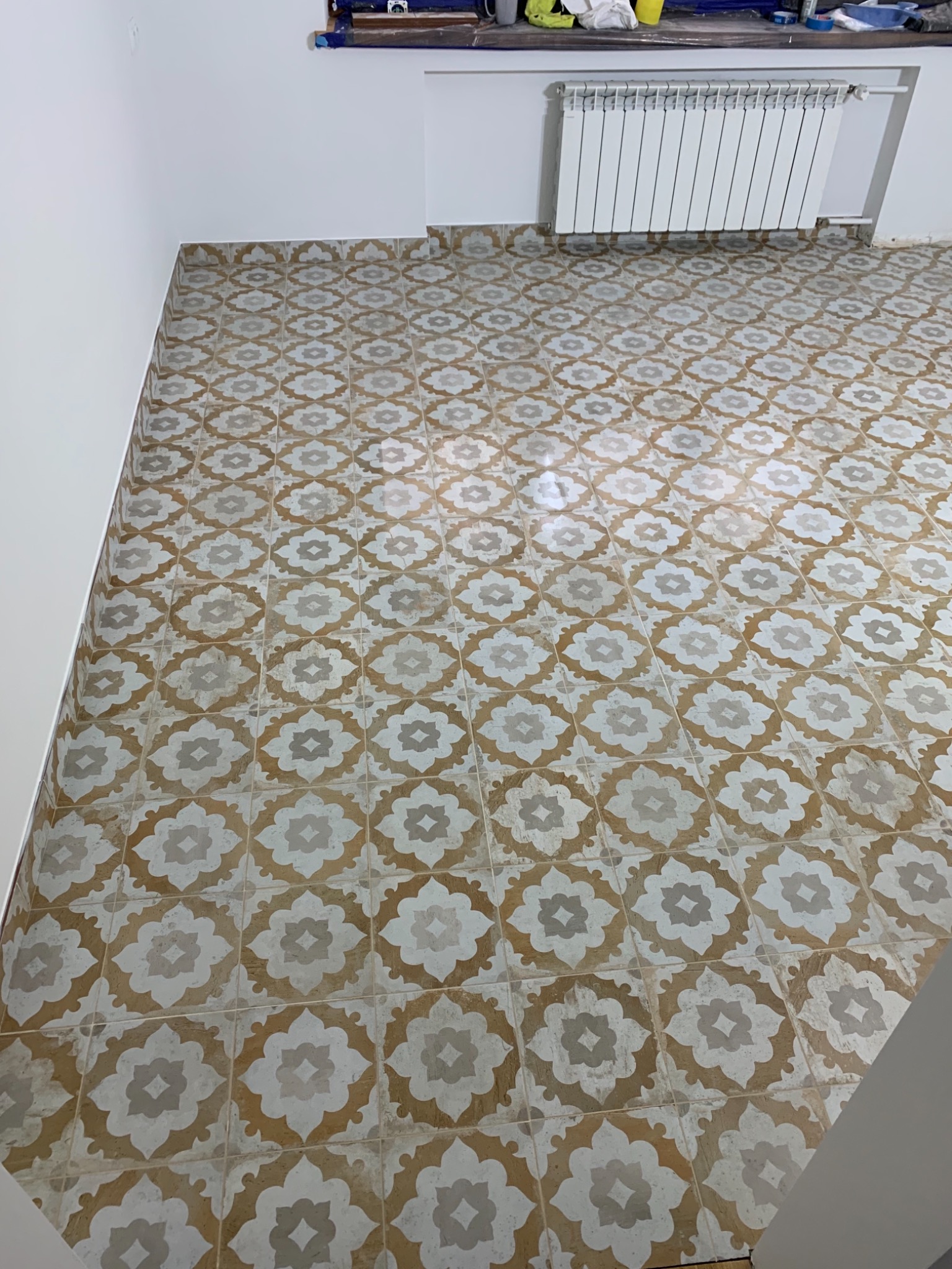 Ułożona podłoga z płytek ceramicznych w geometryczny wzór kwiatowy, widoczny grzejnik i fragment ściany