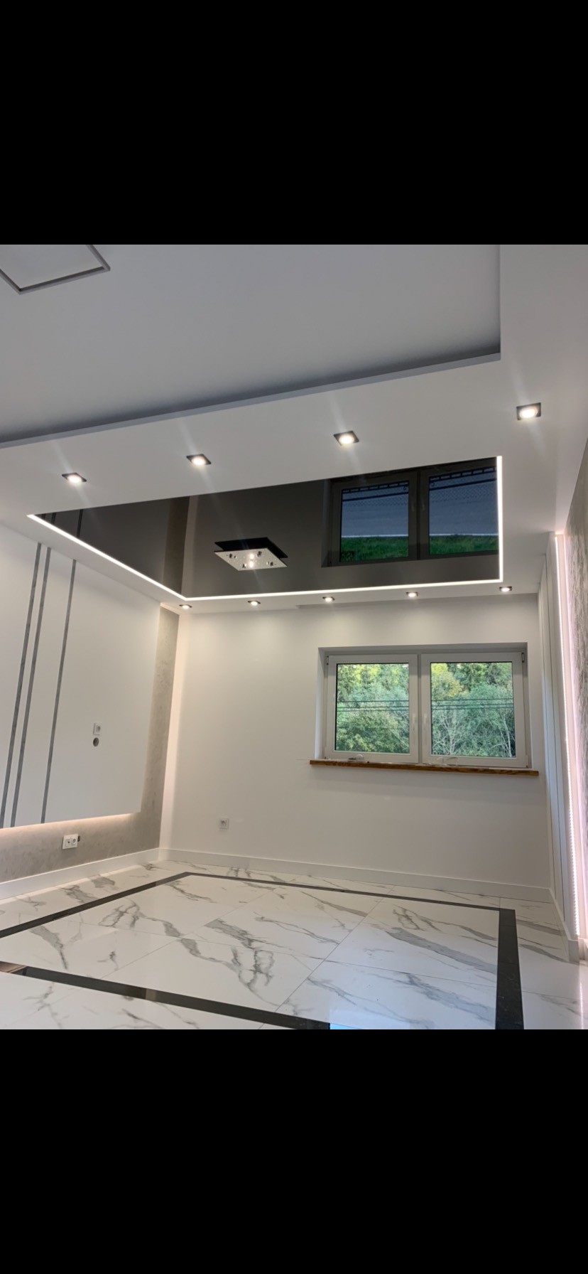 Pokój z nowoczesnym sufitem podwieszanym z czarnym lustrzanym panelem i oświetleniem LED, białe ściany z dekoracyjnymi pionowymi paskami, marmurowa podłoga z czarnymi akcentami, okno z widokiem...