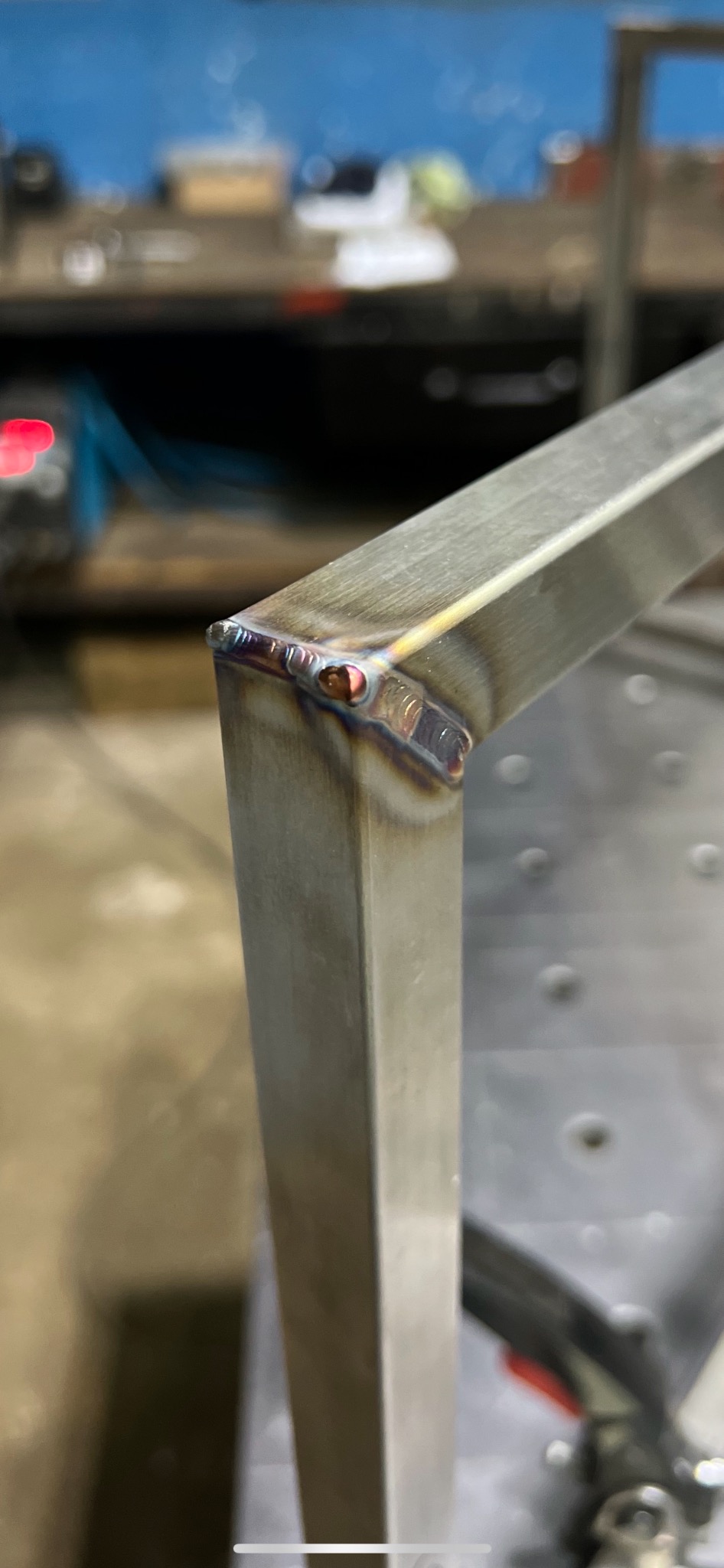 Zbliżenie na spawany narożnik ramy z profili nierdzewnych, widoczne ślady spawania i opalizujące kolory na spoinie.