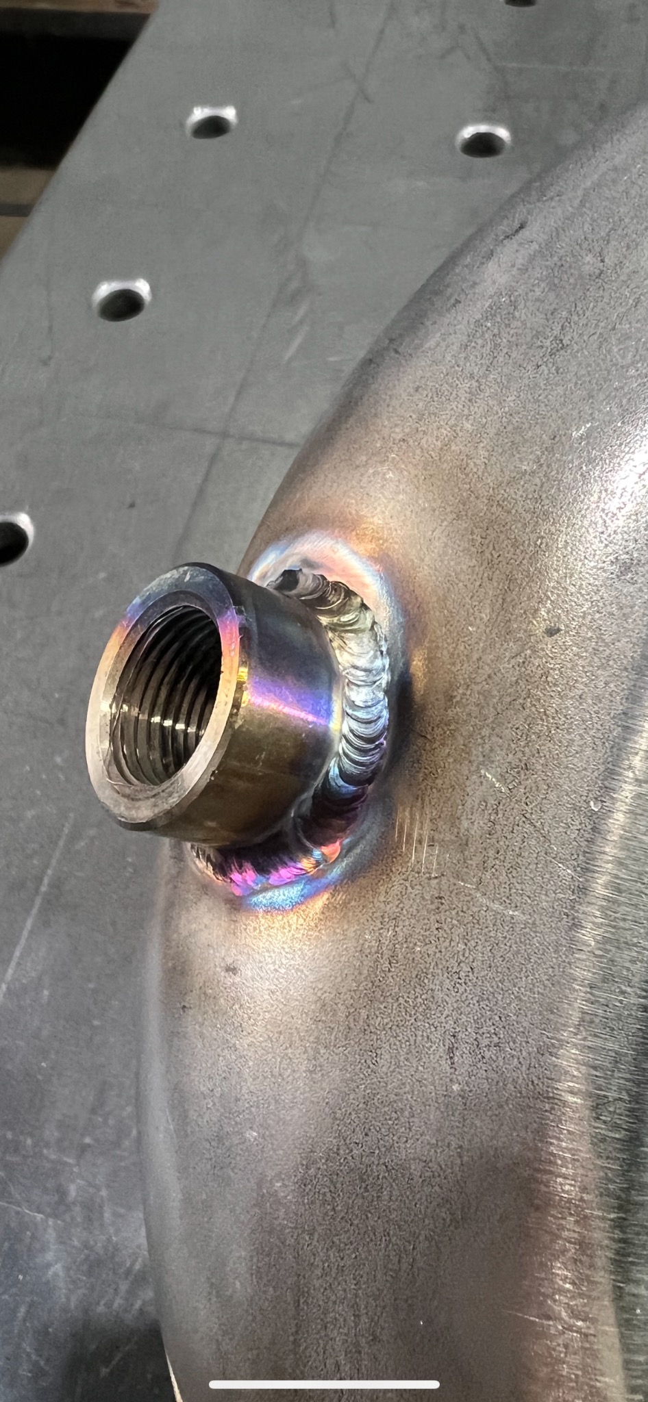 Metalowy zbiornik z precyzyjnym spawem złącza gwintowanego, widoczne tęczowe przebarwienia termiczne na spoinie.