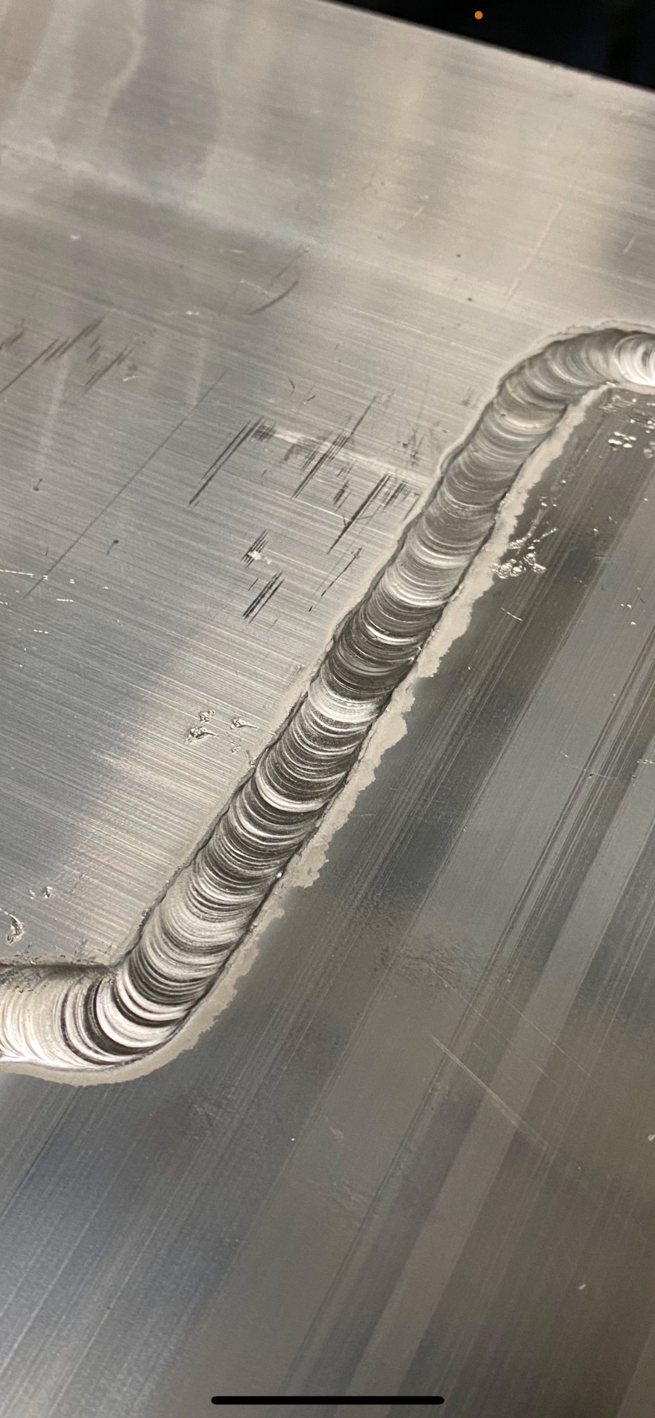 Świeżo wykonany spaw na metalowej powierzchni, widoczne ślady obróbki i drobne zanieczyszczenia.