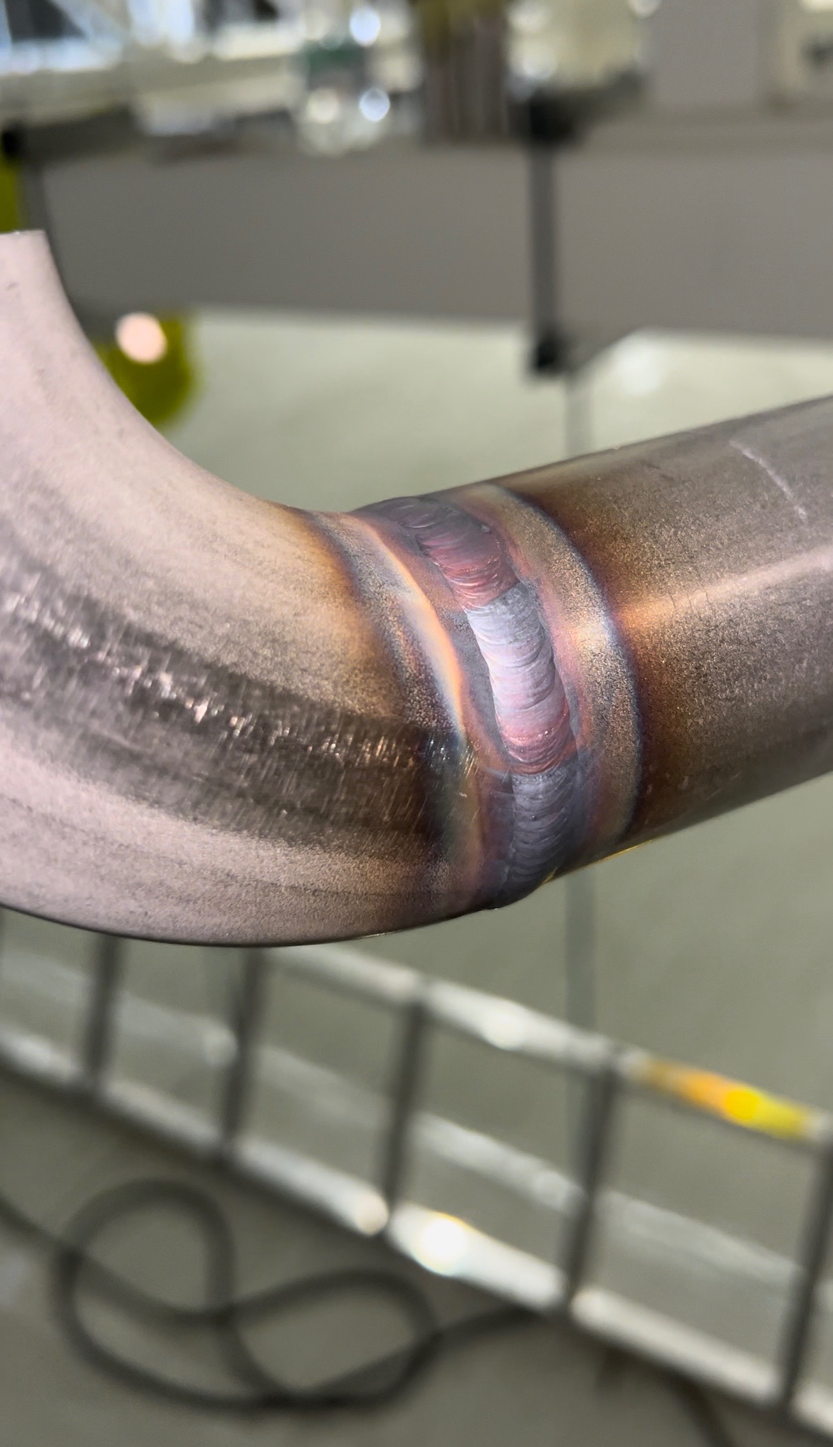 Szczegółowe zbliżenie na spawany element rury ze stali nierdzewnej, widoczna precyzyjna spoina z opalizującymi przebarwieniami termicznymi.