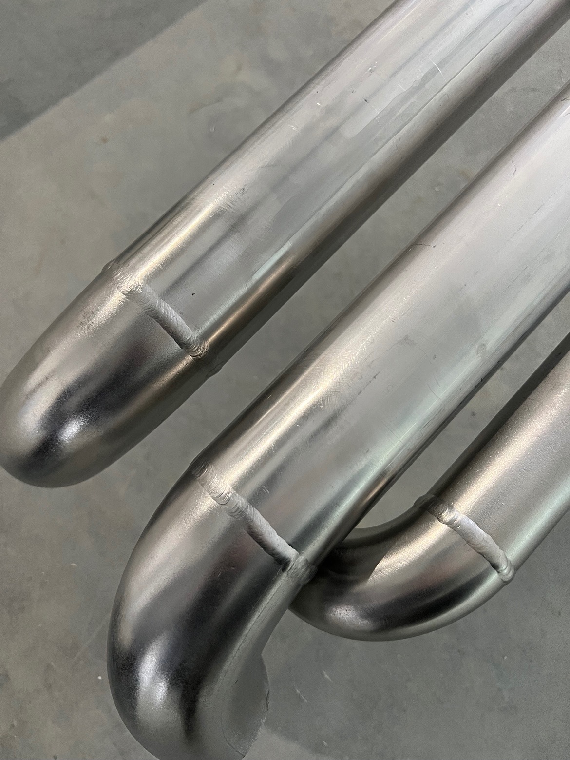 Precyzyjne spawy na zagiętych rurach ze stali nierdzewnej, widoczne detale łączeń i wykończenia powierzchni.