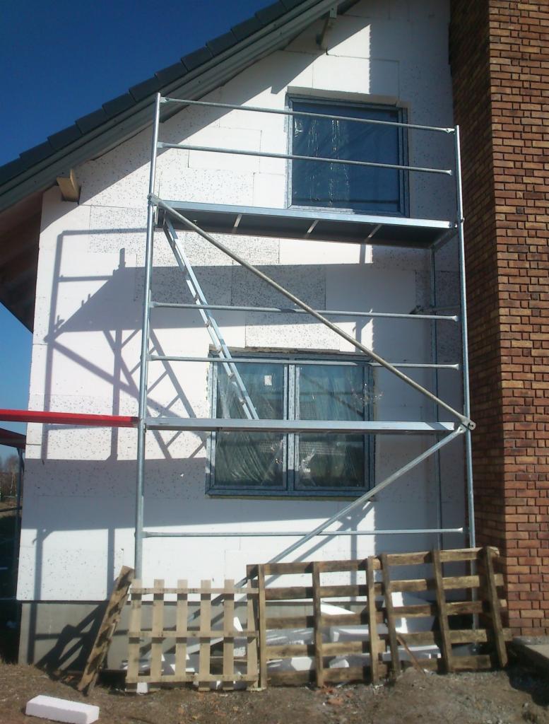 Dom w trakcie docieplania styropianem, widoczne rusztowanie, okna zabezpieczone folią i fragment ceglanego komina.