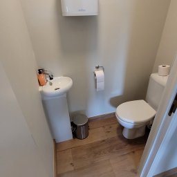 Selfmade Studio Łukasz Jurkowski - Mała łazienka z drewnianą podłogą, umywalką na postumencie z dozownikiem mydła, toaletą i podajnikiem na ręczniki papierowe marki Sabino.