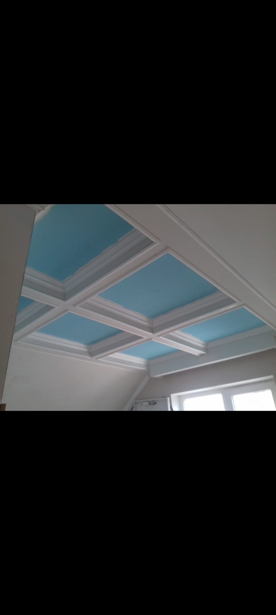 Kasetonowy sufit z białymi listwami i błękitnymi polami, widok z dołu, częściowo widoczne okno i ściana.