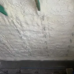 Poddasze ocieplone pianką PUR, widoczne metalowe elementy mocujące oraz drewniana belka stropowa w kolorze zielonym.