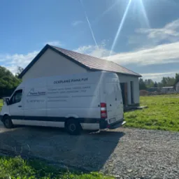 Biały samoch&oacute;d dostawczy z napisem 'Ocieplanie Pianą PUR' na tle budowanego domu jednorodzinnego w słoneczny dzień.