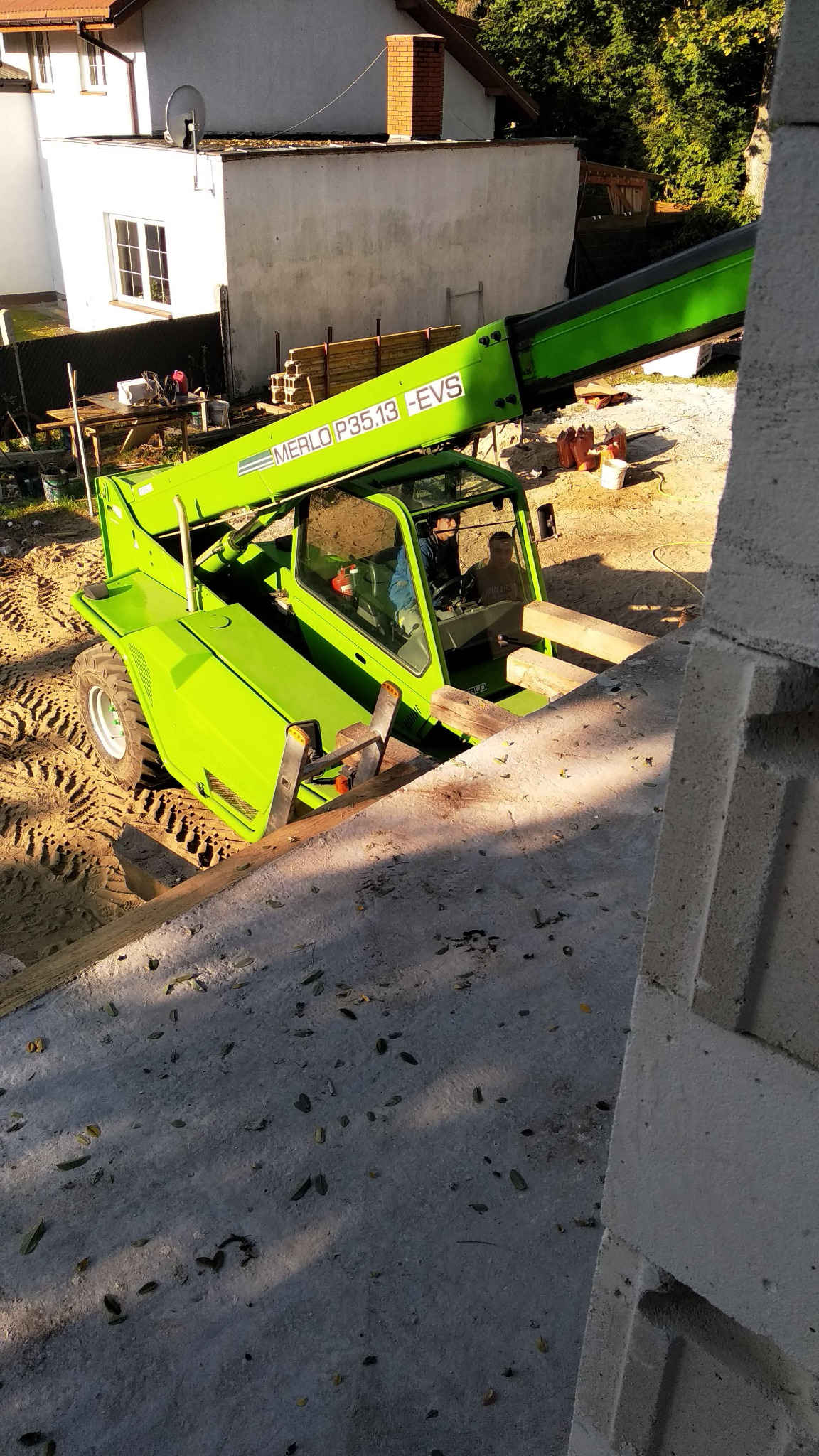 Zielona ładowarka teleskopowa Merlo P35.13 -EVS na placu budowy, widoczna z góry, z elementami konstrukcji murowanej w pierwszym planie.