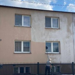 SolarCare BORUSIAK GRZEGORZ - Pracownik z długim uchwytem czyści elewację budynku, widoczna różnica między umytą a brudną powierzchnią, cztery okna w kadrze.