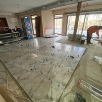 Układanie wielkoformatowych płytek na podłodze w obiekcie w Lęborku. Widoczne krzyżyki dystansowe, narzędzia glazurnicze i częściowo ułożona powierzchnia. W tle okna i elementy konstrukcyjne budynku.