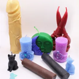 Zestaw różnorodnych, ręcznie robionych świec ozdobnych w kształcie fallusa, księżyca z twarzą, kotów i cylindrów, w odcieniach złota, zieleni, niebieskiego, fioletu, czerwieni, brązu i czerni,...