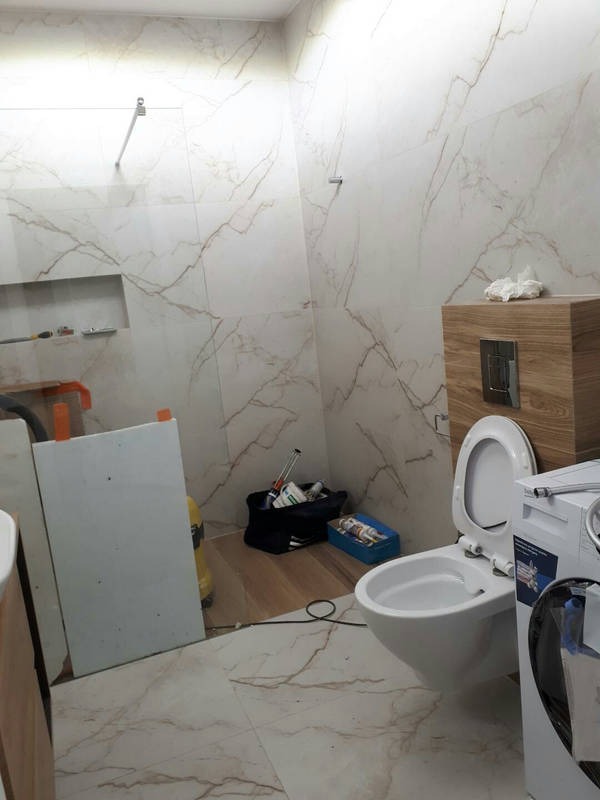 Bidet wiszący z otwartą klapą w trakcie montażu w łazience wykończonej płytkami imitującymi marmur, widoczne narzędzia i akcesoria instalacyjne.