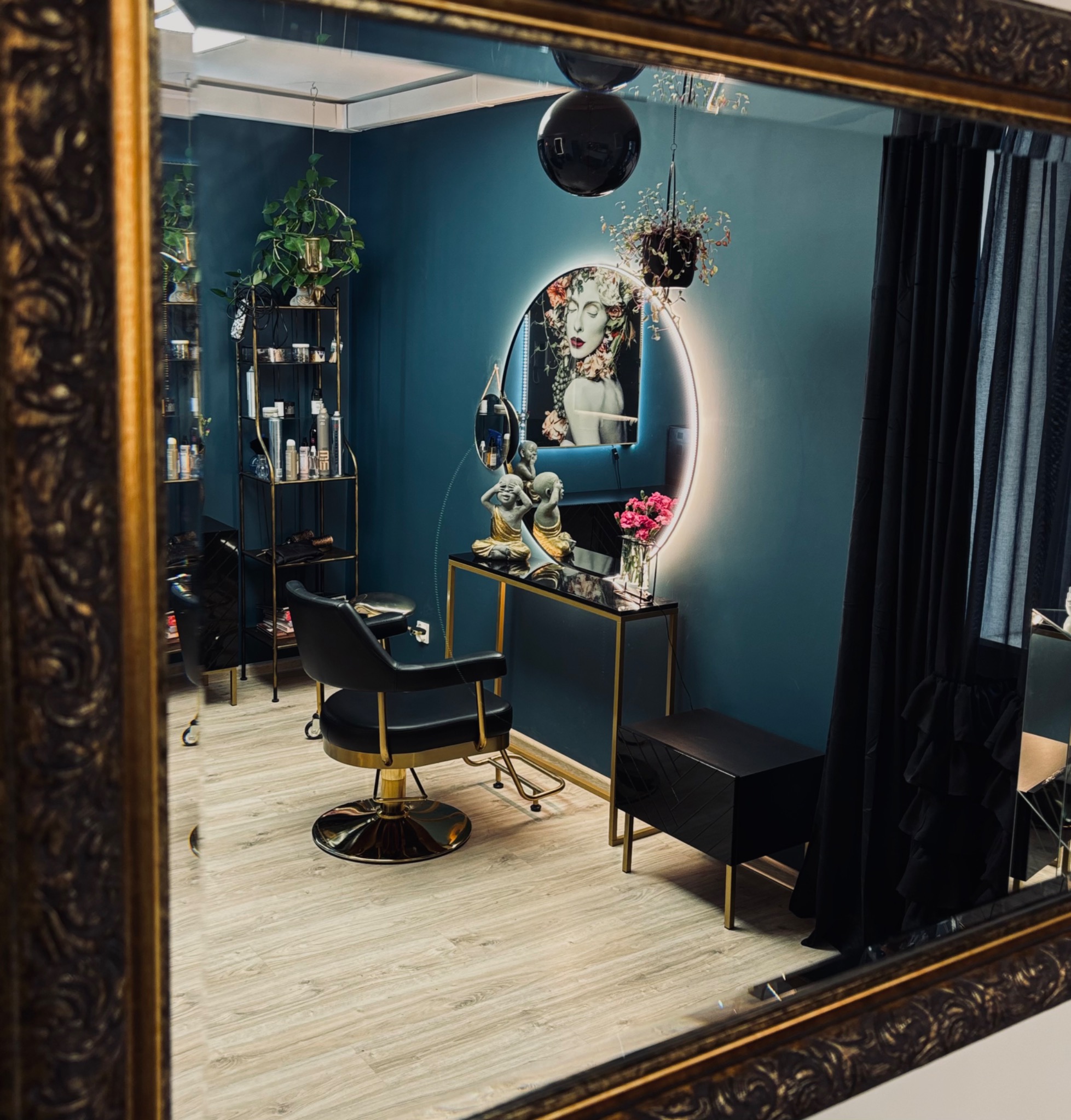 Eleganckie wnętrze salonu, odbicie w ozdobnym lustrze, z czarnym fotelem fryzjerskim, złotymi akcentami, dekoracyjnym oświetleniem i turkusowymi ścianami.