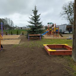 Wojcik - Nowo wybudowany plac zabaw z piaskownicami, drabinkami i zjeżdżalniami, otoczony świeżo przekopaną ziemią i młodymi drzewkami.