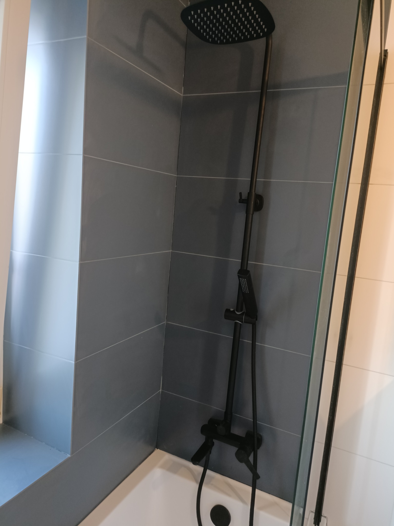 Nowoczesny zestaw prysznicowy w kolorze czarnym na tle szarych płytek w kabinie prysznicowej z elementami białej wanny.