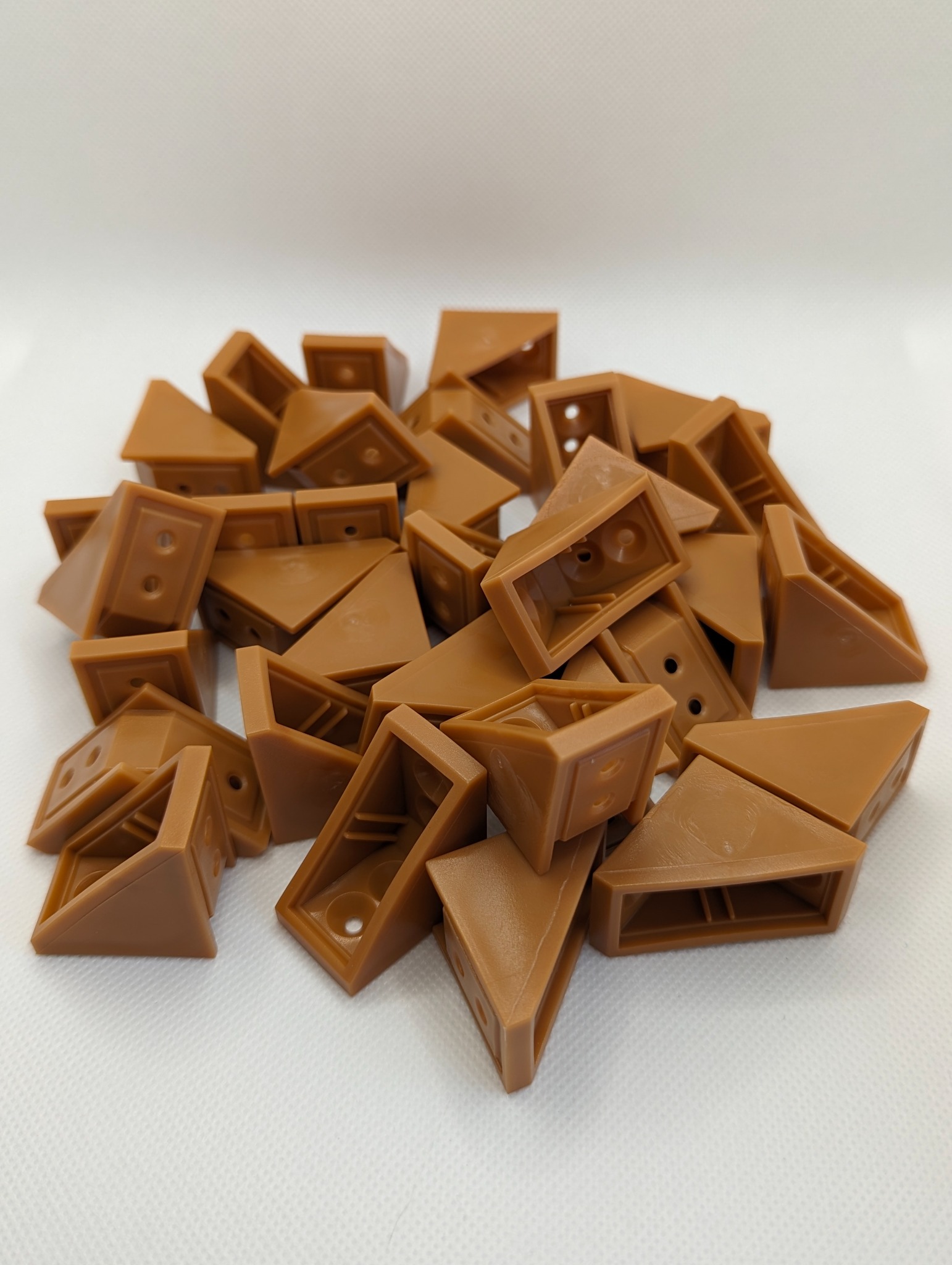 Stos brązowych, plastikowych narożników z otworami na śruby, ułożonych na białym tle.