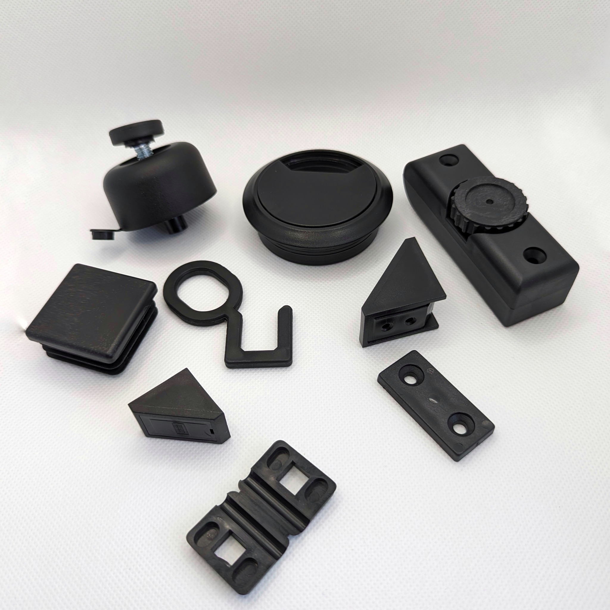 Zestaw czarnych, plastikowych komponentów o różnych kształtach i rozmiarach, ułożonych na białym tle. Widoczne elementy to m.in. zaślepki, regulatory, łączniki i inne detale montażowe.