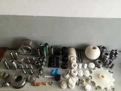 Zestaw różnorodnych, precyzyjnie obrobionych metalowych i plastikowych elementów, w tym tuleje, śruby, nakrętki, koła zębate i kuliste elementy, ułożonych na szarym tle, prezentujący szeroki zakres...