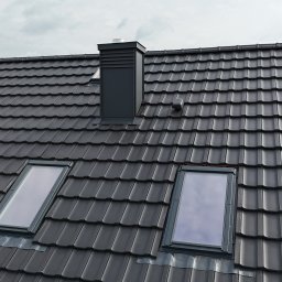 Uaługi Blacharsko-Dekarskie ART-Dachy - Grafitowy dach z dachówki ceramicznej z dwoma oknami połaciowymi i kominem, widok z góry. Nowoczesne pokrycie dachowe w stonowanej kolorystyce.