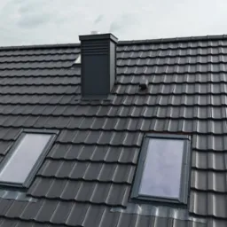 Grafitowy dach z dachówki ceramicznej z dwoma oknami połaciowymi i kominem, widok z góry. Nowoczesne pokrycie dachowe w stonowanej kolorystyce.