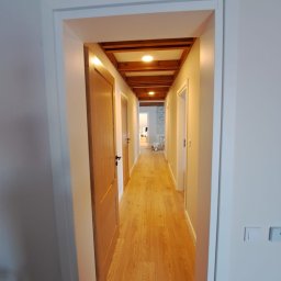 LUXBUD ŁUKASZ IGNACIUK - Długi korytarz z drewnianą podłogą i widoczną drewnianą konstrukcją sufitu z oświetleniem punktowym, świeżo pomalowane ściany w jasnym odcieniu.