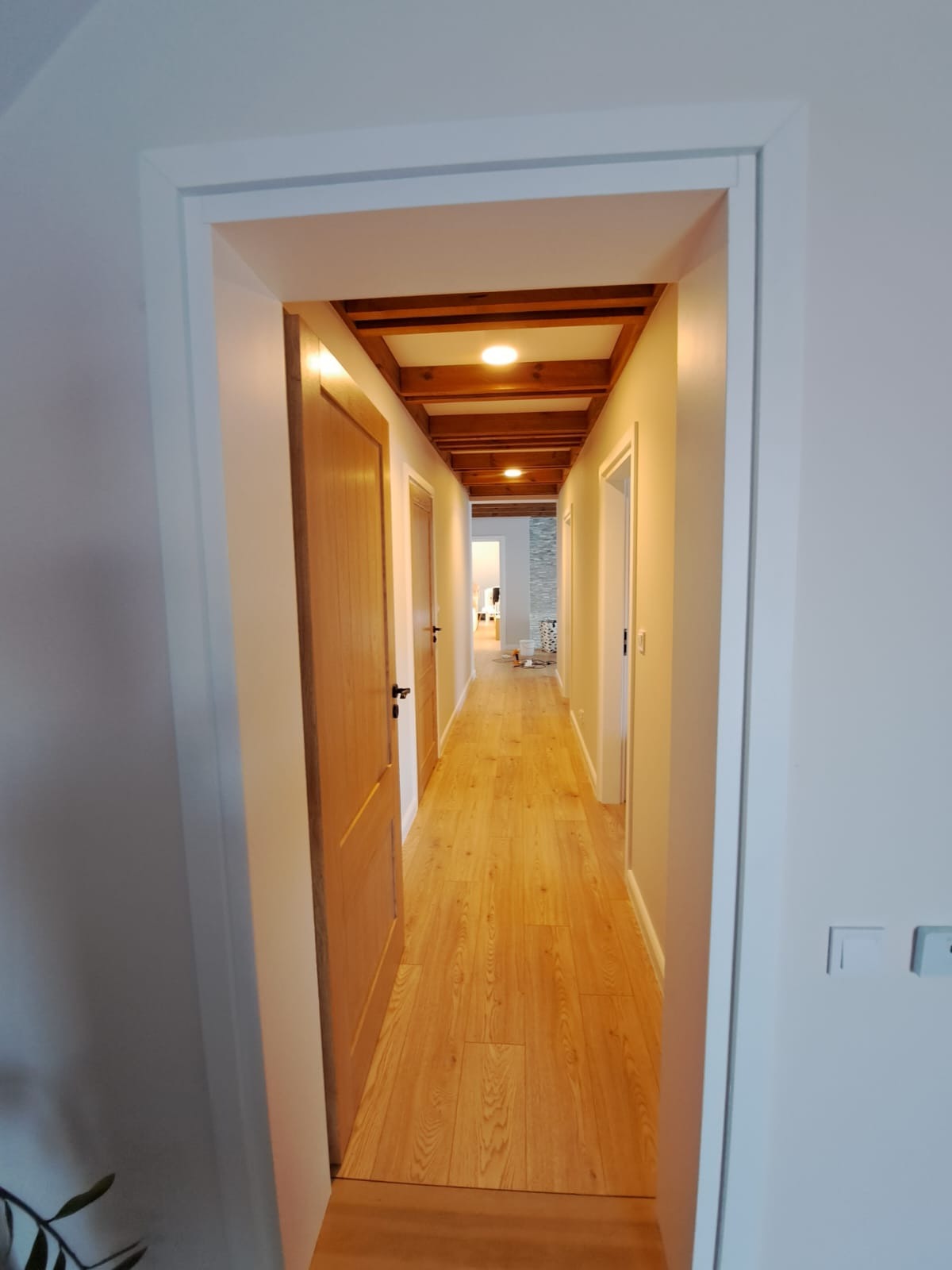 Długi korytarz z drewnianą podłogą i widoczną drewnianą konstrukcją sufitu z oświetleniem punktowym, świeżo pomalowane ściany w jasnym odcieniu.