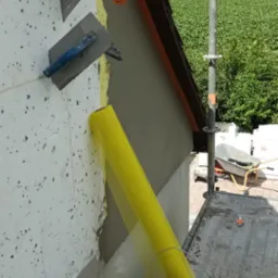 Elewacja budynku w trakcie ocieplania, widoczne płyty styropianowe, siatka elewacyjna w kolorze żółtym, szpachla oraz rusztowanie.