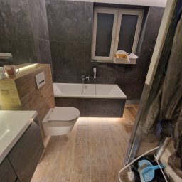 Oko - Nowoczesna łazienka w trakcie wykańczania, z podświetlaną wanną, wiszącą toaletą i drewnopodobną zabudową umywalki, widoczne narzędzia i materiały budowlane.