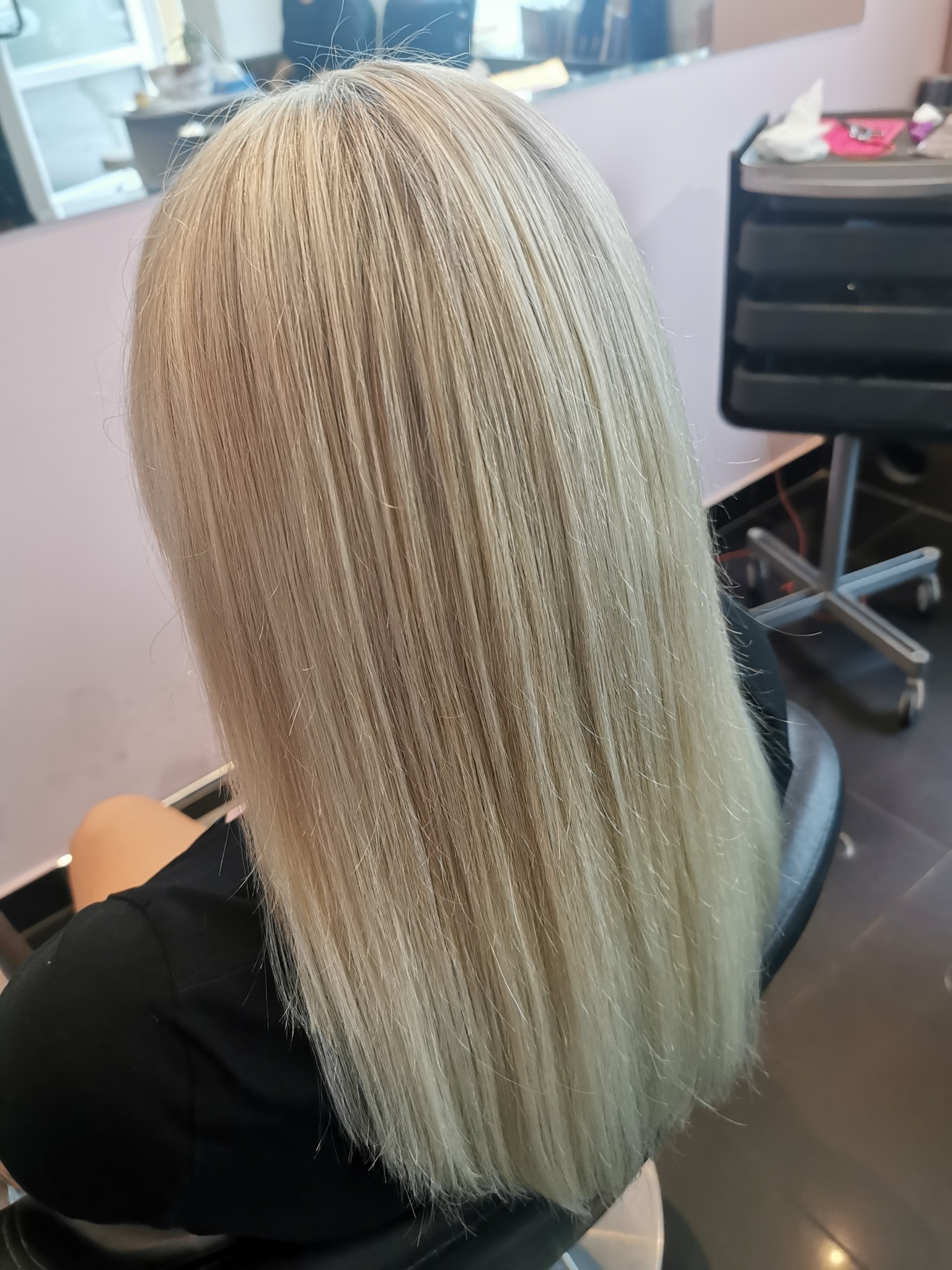 Długie, proste, platynowe włosy klientki po koloryzacji w salonie fryzjerskim, widok z tyłu.