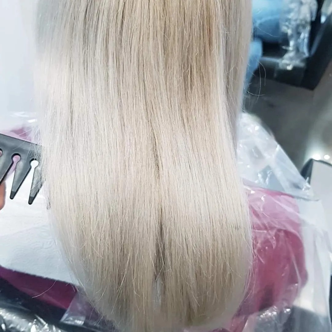 Świeżo rozjaśnione, platynowe włosy klientki rozczesywane czarnym grzebieniem w salonie, widok z tyłu głowy.