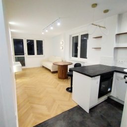 Vitalii Mordvinov - Jasne wnętrze mieszkania po remoncie: parkiet ułożony w jodełkę, białe ściany, minimalistyczne meble i czarny blat kuchenny.