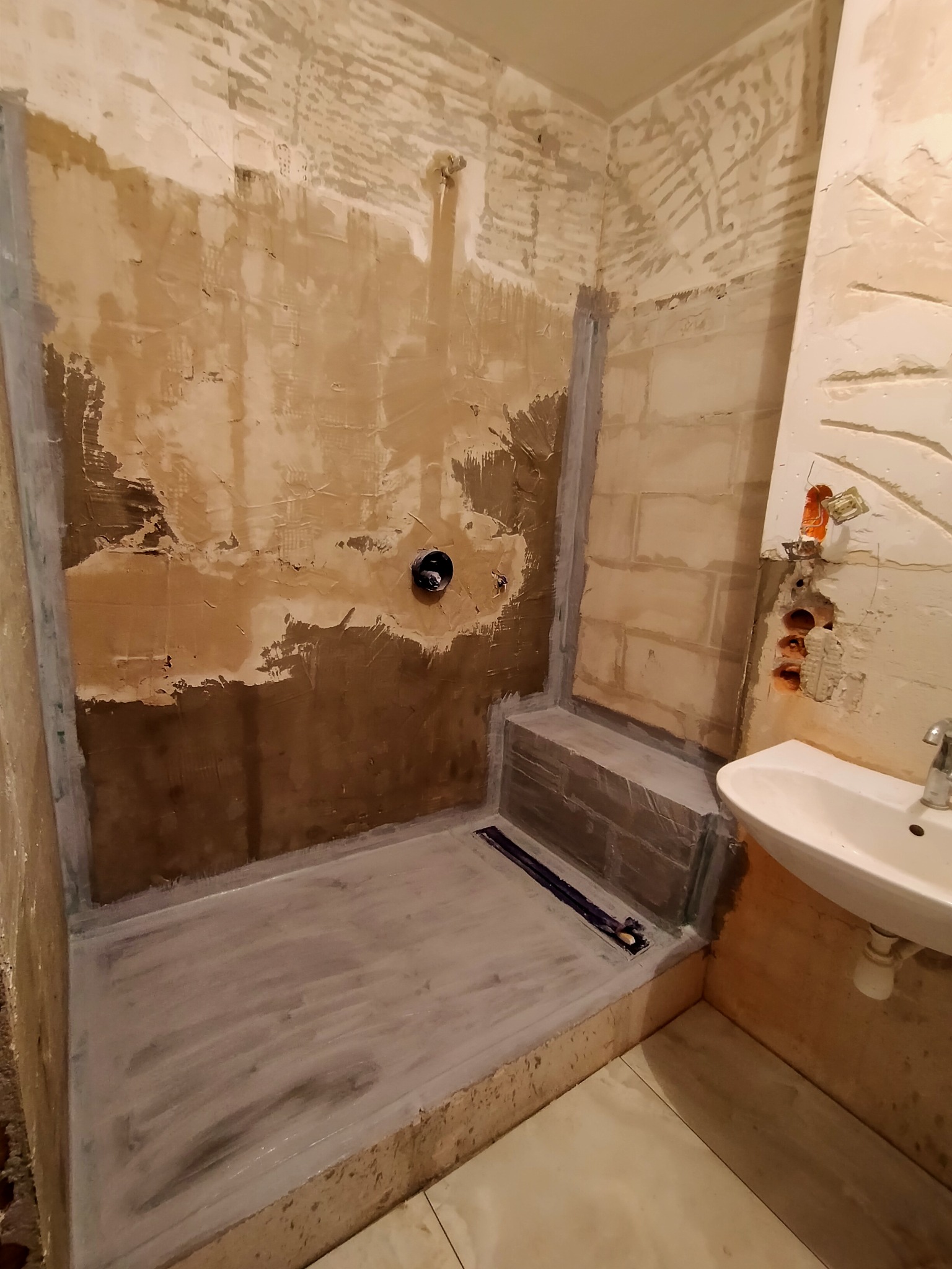 Przygotowanie ścian i podłogi w kabinie prysznicowej do położenia płytek, widoczne zaszpachlowane nierówności, uszczelniona podłoga i ściany, oraz odpływ liniowy.