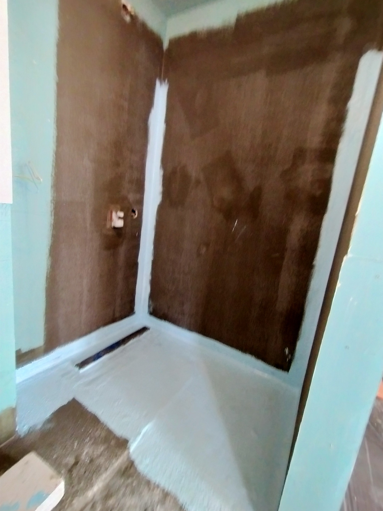 Przygotowanie podłoża w łazience: hydroizolacja ścian i podłogi w narożnikach, widoczny odpływ liniowy.