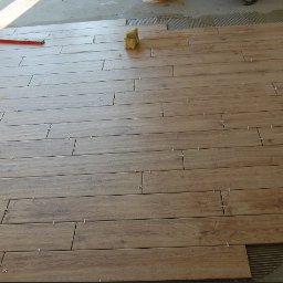 Marcin Rosiak - Układanie podłogi z płytek imitujących drewno, widoczne krzyżyki dystansowe, poziomica i gąbka