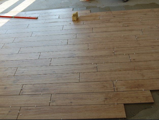 Układanie podłogi z płytek imitujących drewno, widoczne krzyżyki dystansowe, poziomica i gąbka