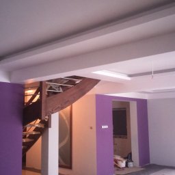 Zakład Remontowo Budowlany Cojg Zbigniew - Wnętrze w trakcie malowania: fioletowe akcenty na ścianach, drewniane schody i sufit z oświetleniem. Widoczne ślady prac remontowych, w tym worki i narzędzia.