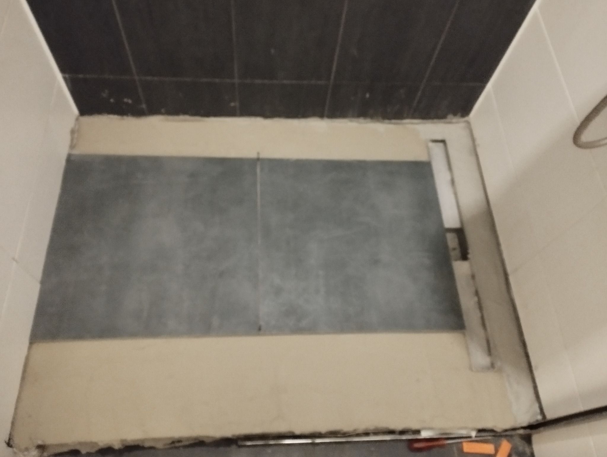 Przygotowanie podłoża pod prysznic z odpływem liniowym, widoczne płytki podłogowe i fragment ściany z glazurą.