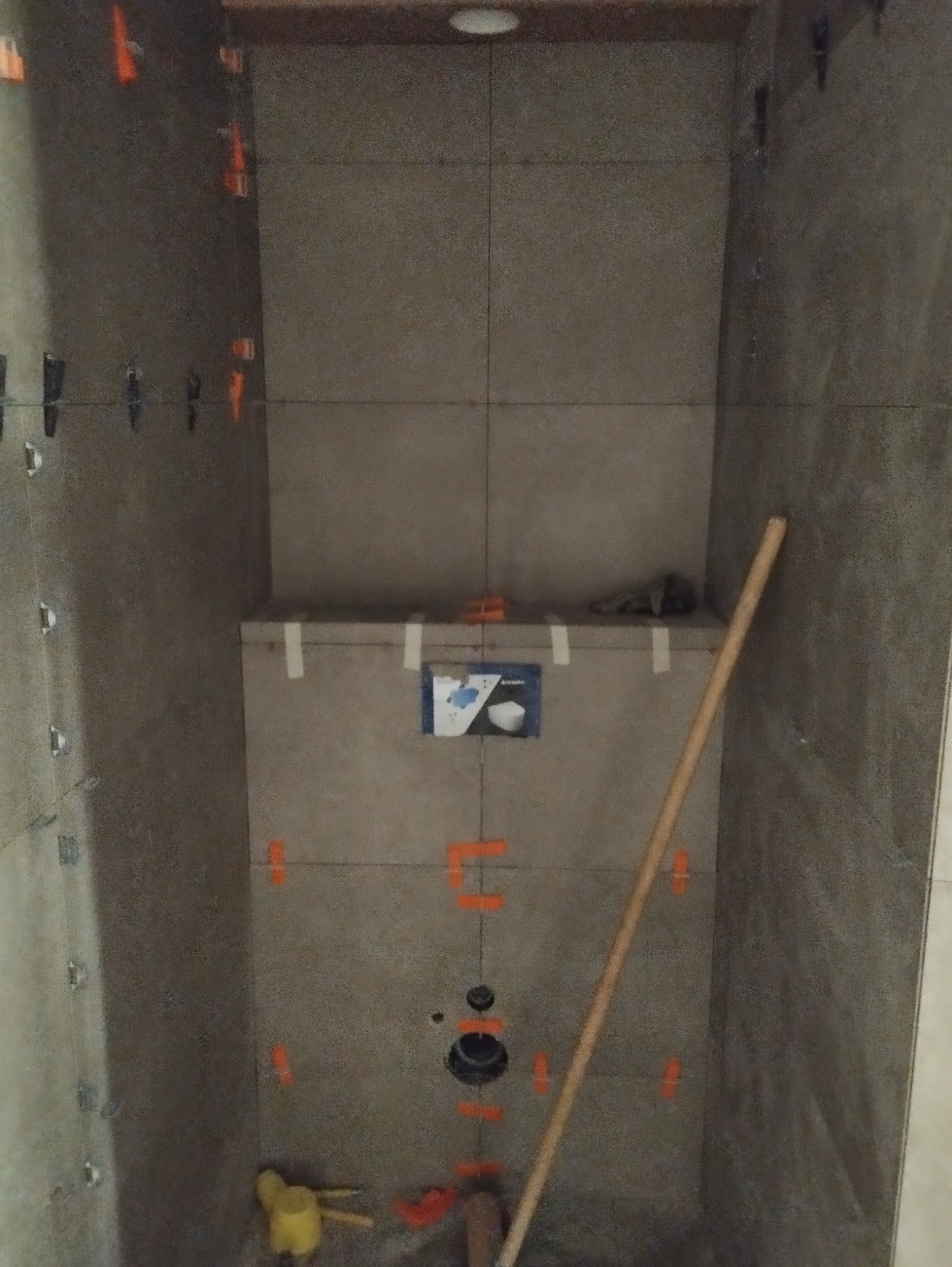 Montaż płytek ceramicznych w łazience z widocznymi krzyżykami dystansowymi i poziomowaniem, przygotowanie do instalacji toalety podtynkowej