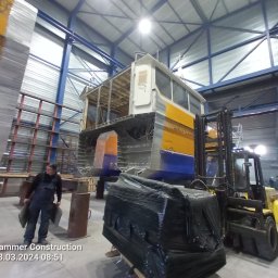 Firma Usługowa Marcin Jażdżewski - Konstrukcja stalowa modułu budynku w hali produkcyjnej, transportowana wózkiem widłowym, pracownik w ubraniu roboczym w tle.