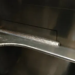 Szczegółowe zbliżenie spoiny TIG na nierdzewnej konstrukcji, widoczne charakterystyczne łuski spawalnicze i precyzyjne połączenie blach.