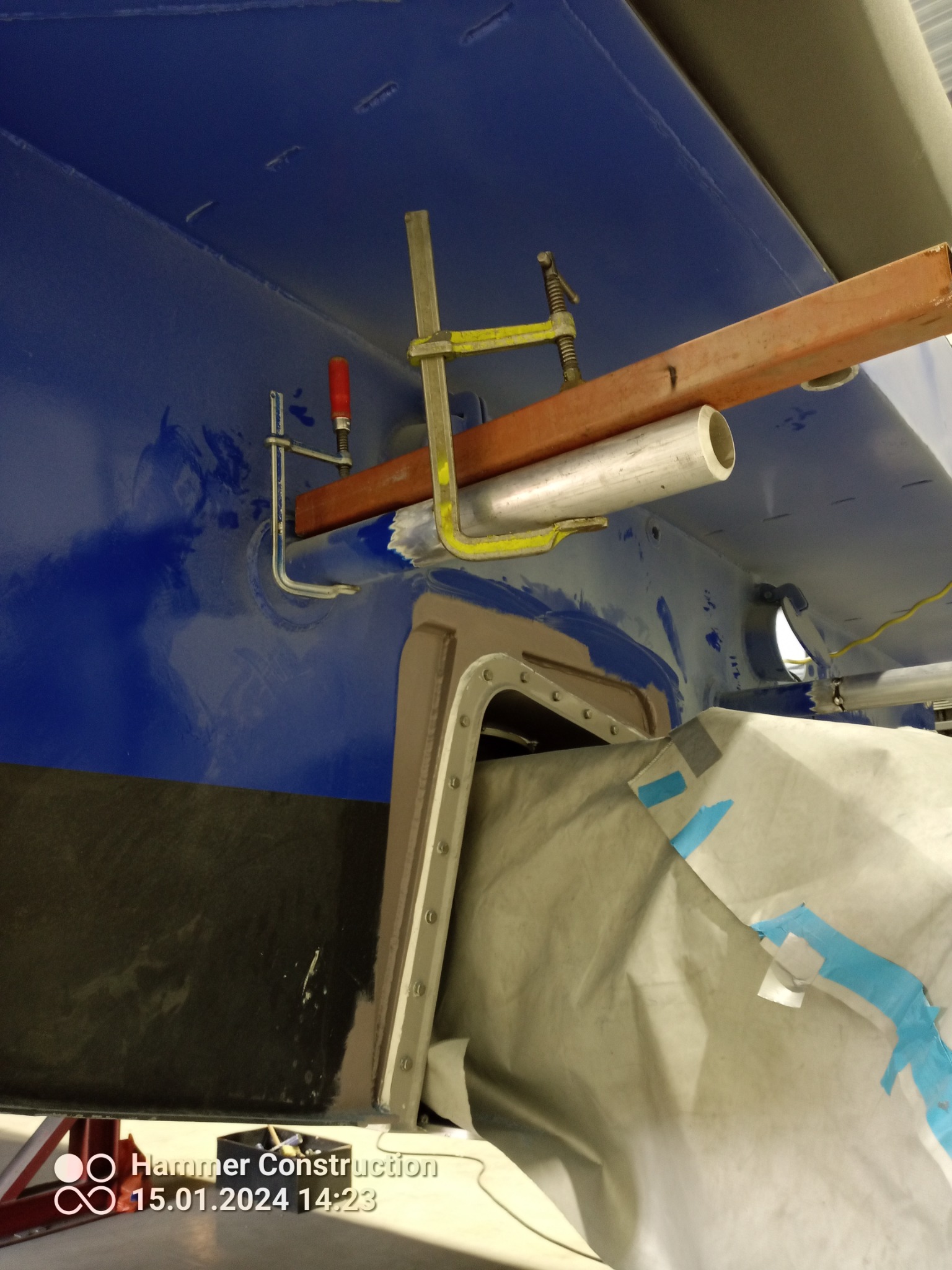 Fragment konstrukcji metalowej w trakcie naprawy, zabezpieczony folią, z widocznymi śladami spawania i zaciskami stolarskimi