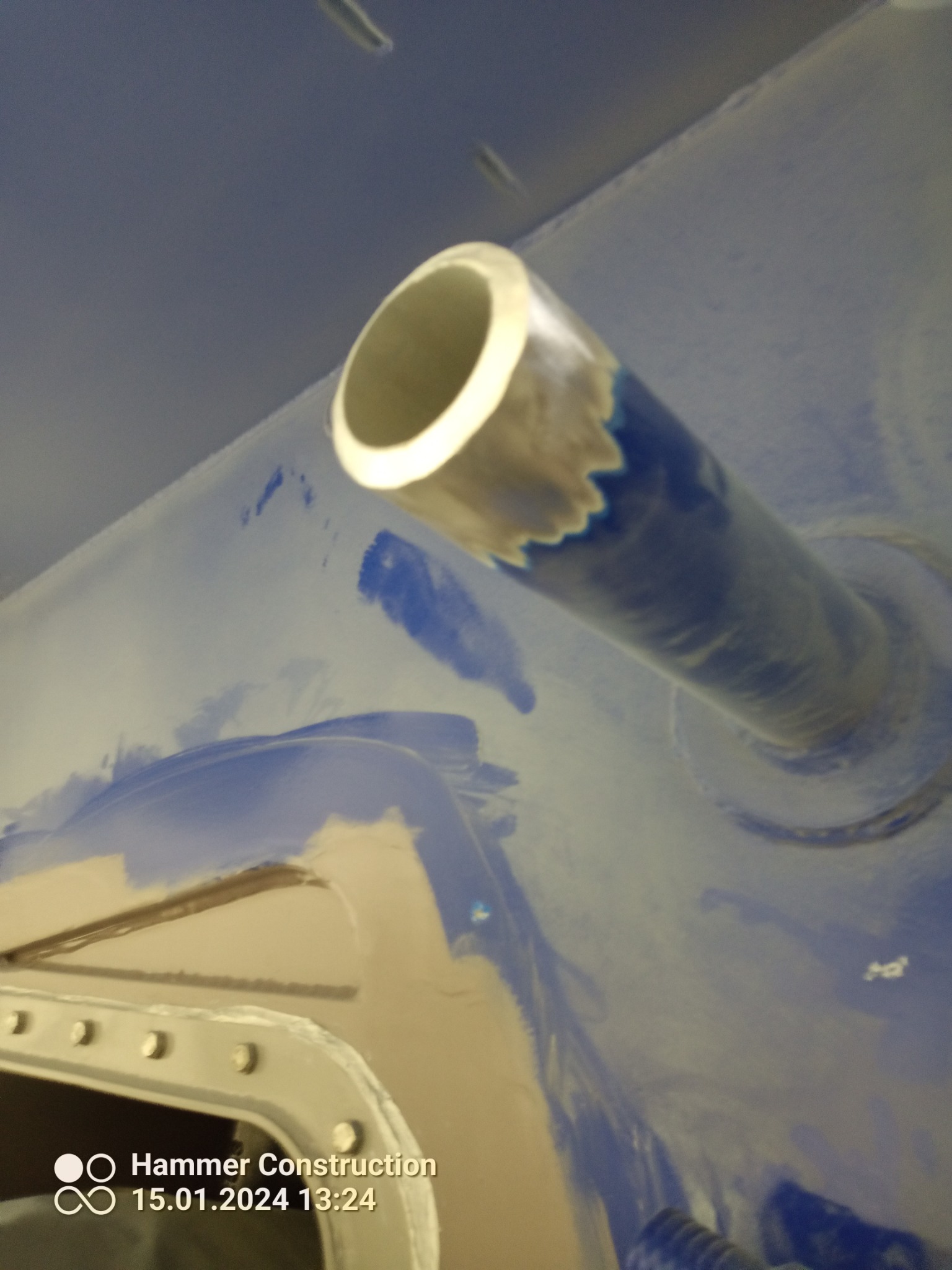 Surowe ujęcie rury wystającej z niebieskiej, metalowej powierzchni w Liniewie, z widocznymi śladami obróbki i niedoskonałościami wykończenia.