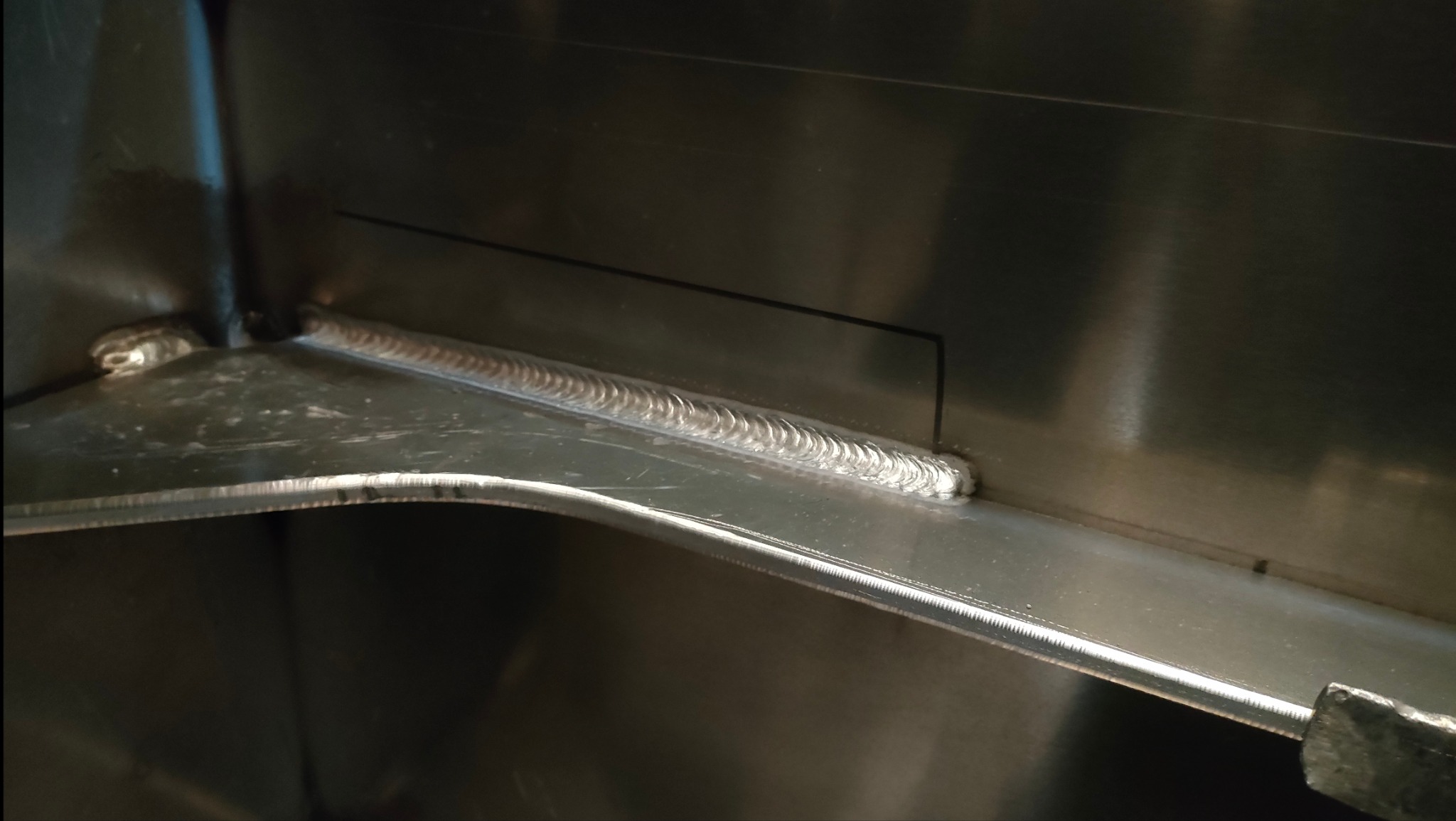 Szczegółowe zbliżenie spoiny TIG na nierdzewnej konstrukcji, widoczne charakterystyczne łuski spawalnicze i precyzyjne połączenie blach.