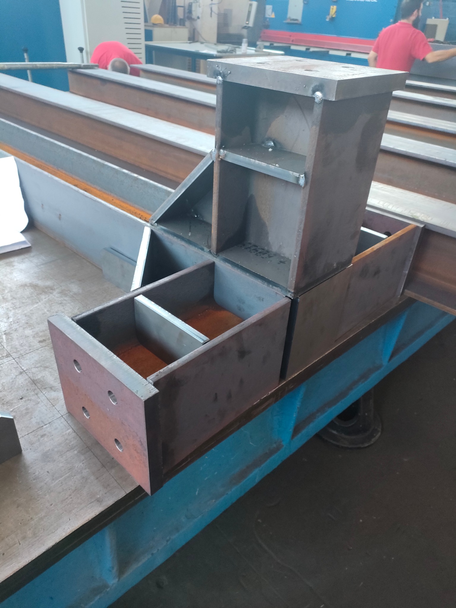 Konstrukcja spawana z profili stalowych, widoczne spawy, surowy metal, elementy połączone pod kątem prostym, na stole warsztatowym.