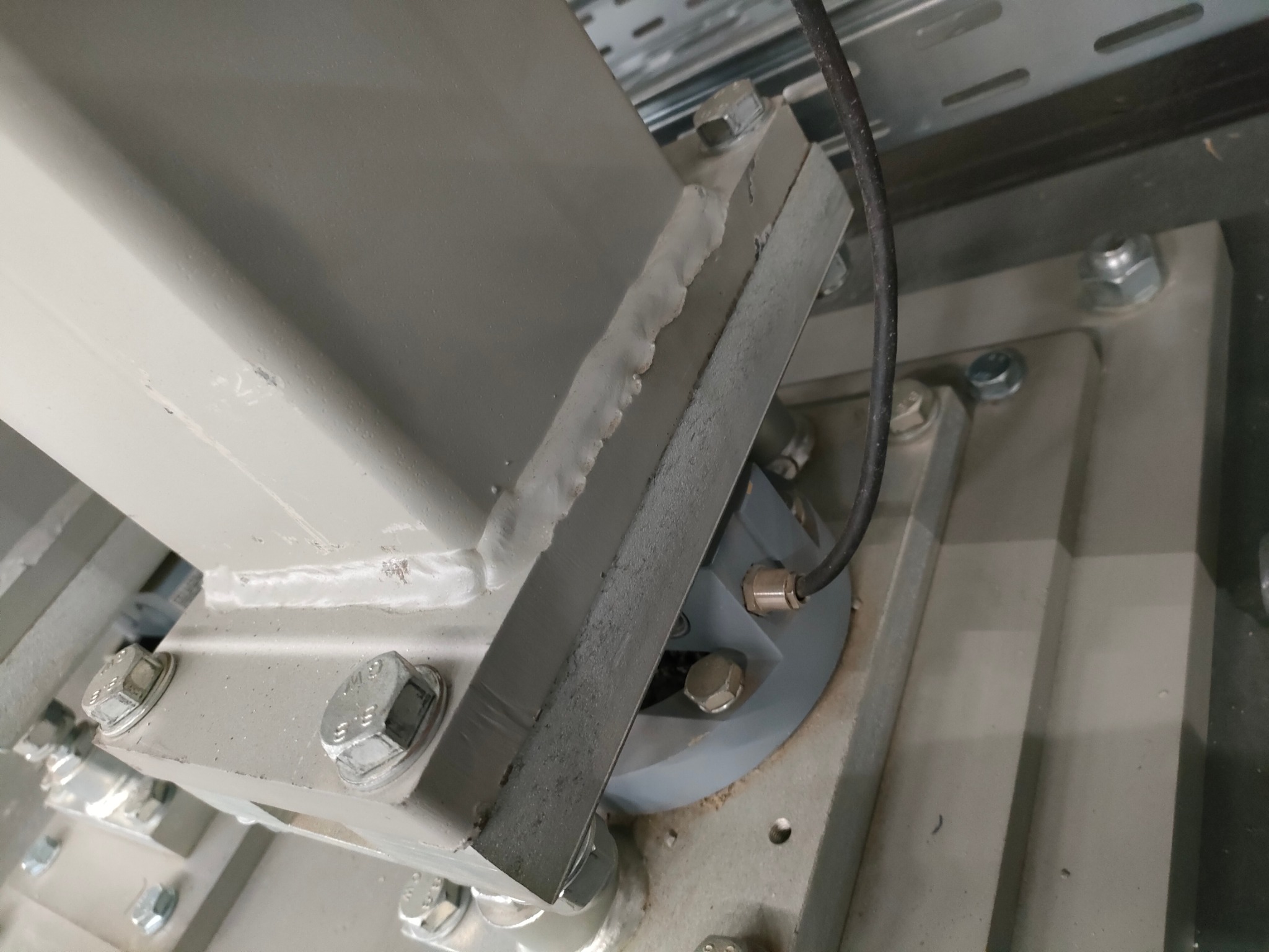 Szczegółowe ujęcie spawu łączącego metalowe elementy konstrukcyjne, widoczne ślady po spawaniu i śruby mocujące.