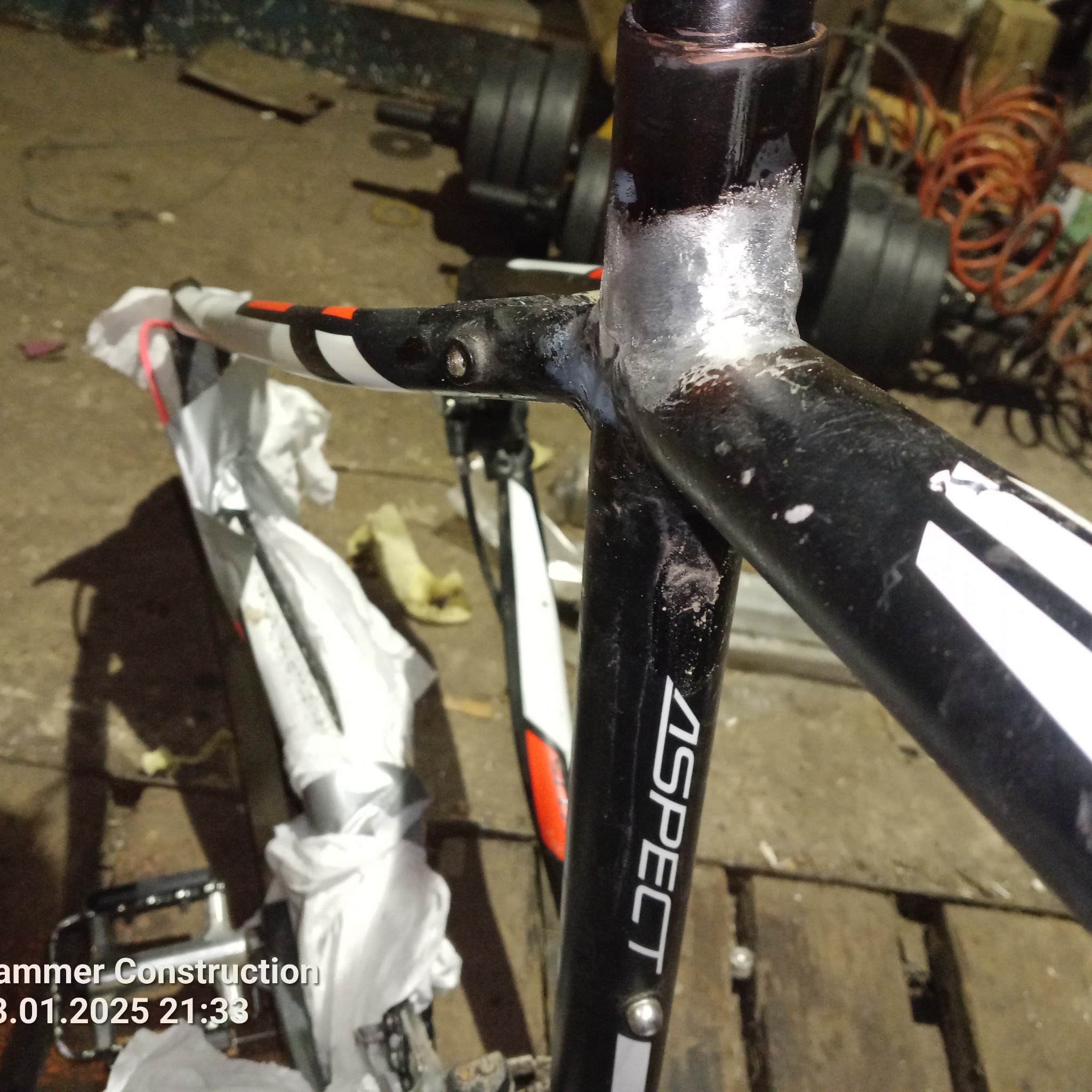 Fragment ramy rowerowej marki Aspect po spawaniu, widoczne ślady obróbki i czyszczenia, w tle warsztat z narzędziami i akcesoriami.