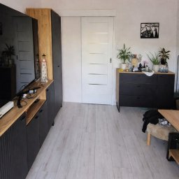 Konrad Szlaga - Jasne panele podłogowe w salonie z czarnymi meblami i przesuwnymi drzwiami. Minimalistyczny wystrój z roślinami i dekoracją ścienną.